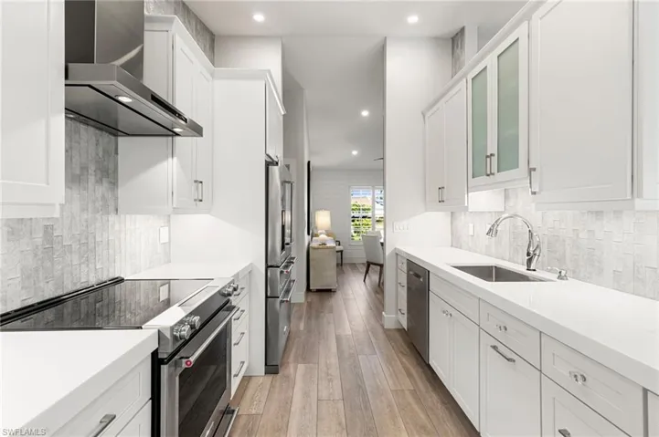 Kitchen with appliances with stainless steel finishes, wall chimney range hood, backsplash, recessed lighting, and white cabinetry