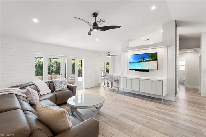 Living room featuring healthy amount of natural light, light wood-type flooring, a ceiling fan, wood walls, and recessed lighting