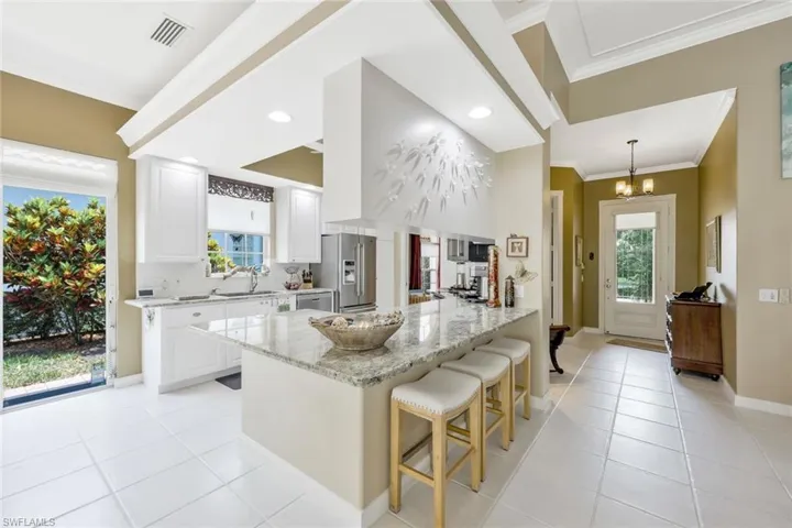 Kitchen featuring a kitchen breakfast bar, high end refrigerator, white cabinetry, and light stone counters