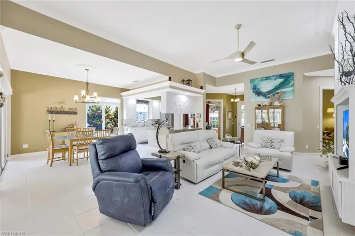 Tiled living room with sink, crown molding, and ceiling fan with notable chandelier
