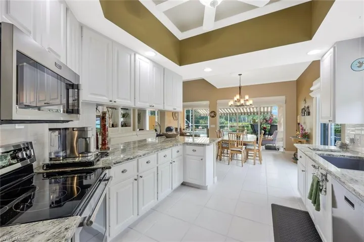 Kitchen featuring light tile flooring, ceiling fan with notable chandelier, backsplash, white cabinetry, and appliances with stainless steel finishes