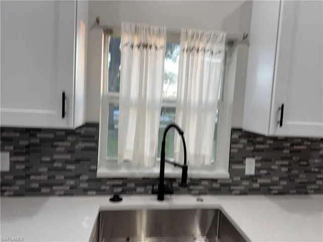 Kitchen with stove, white cabinets, backsplash, and light tile patterned floors