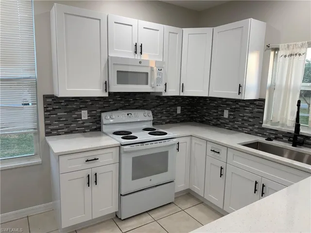 Kitchen featuring backsplash, freestanding refrigerator, light stone countertops, white cabinets, and light tile patterned floors