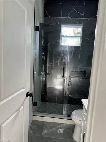 Bathroom featuring a shower with door, toilet, vanity, and tile patterned floors