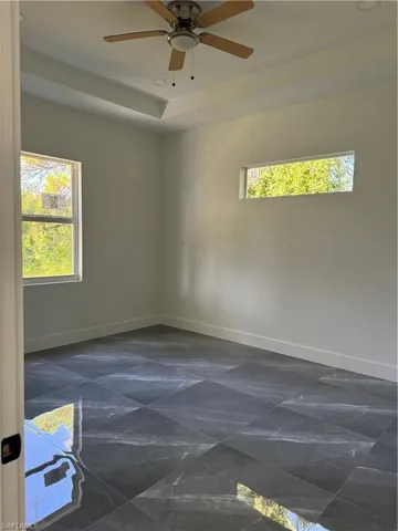 Tiled empty room featuring ceiling fan and a tray ceiling