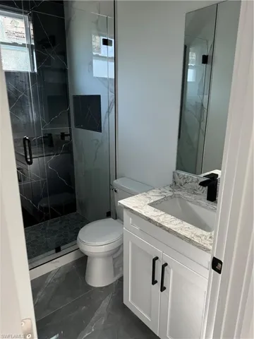 Bathroom featuring tile patterned flooring, toilet, vanity, and a shower with shower door