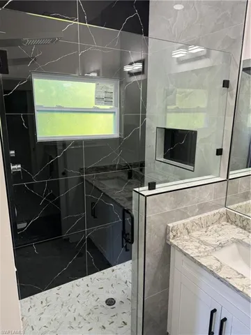Bathroom featuring walk in shower, vanity, and tile walls