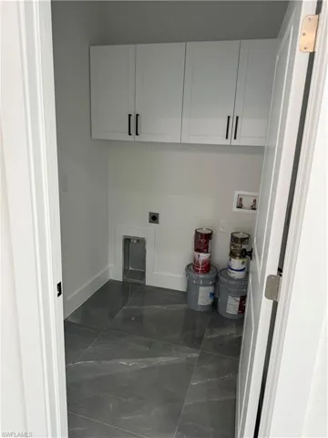 Clothes washing area featuring hookup for an electric dryer, dark tile patterned flooring, cabinets, and hookup for a washing machine