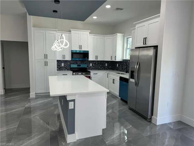 Kitchen featuring tasteful backsplash, hanging light fixtures, white cabinets, appliances with stainless steel finishes, and a center island
