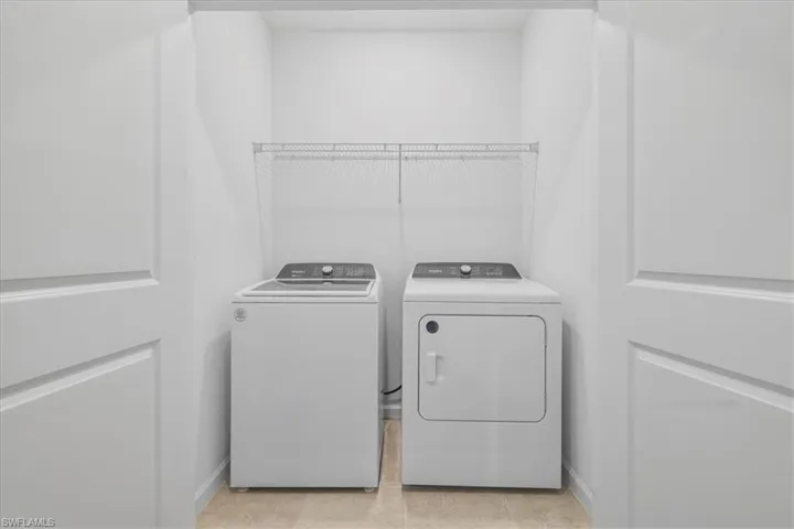Laundry room with washer and clothes dryer, light tile patterned floors, and baseboards
