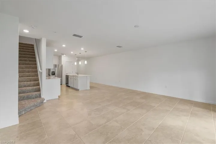Unfurnished living room featuring stairs, light tile patterned floors, recessed lighting, a sink, and baseboards