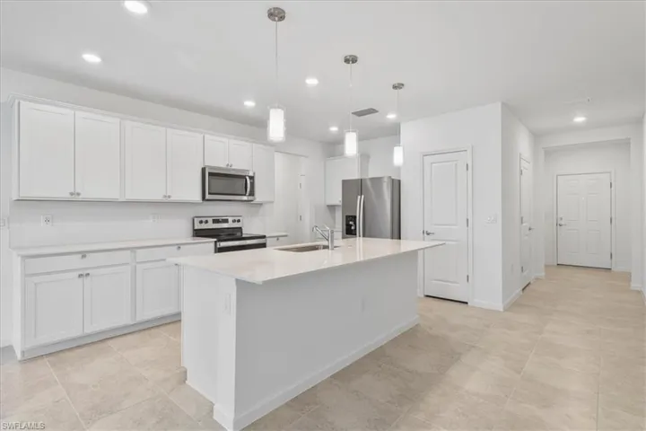 Kitchen with stainless steel appliances, a sink, a center island with sink, white cabinets, and recessed lighting