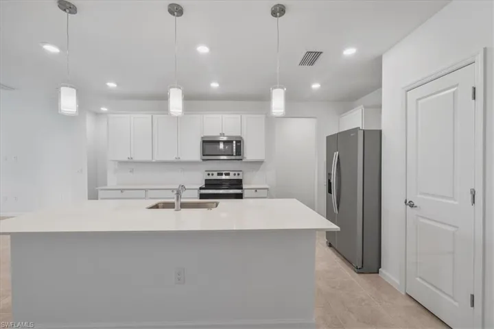Kitchen featuring stainless steel appliances, a sink, white cabinets, light countertops, and a center island with sink