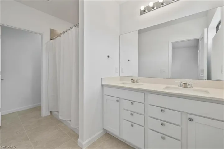 Full bath with double vanity, tile patterned floors, baseboards, and a shower with shower curtain