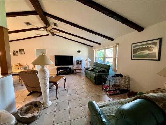 Living room featuring vaulted ceiling with beams, light tile patterned flooring, and ceiling fan