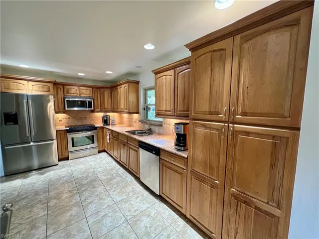 Kitchen with sink, decorative backsplash, light GRANITE countertops, light tile patterned floors, and appliances with stainless steel finishes