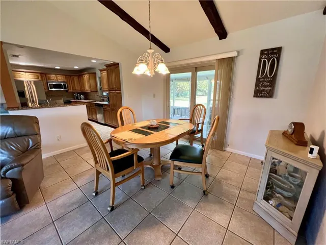 Tiled dining area featuring lofted ceiling with beams and an inviting chandelier
