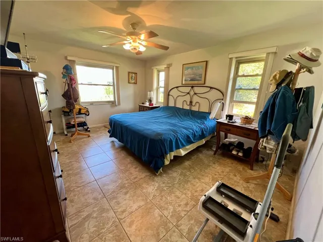 Primary bedroom with ceiling fan, light tile patterned floors, and multiple windows