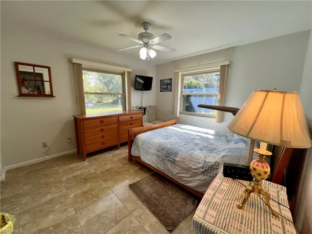 Tiled guest bedroom featuring ceiling fan and multiple windows