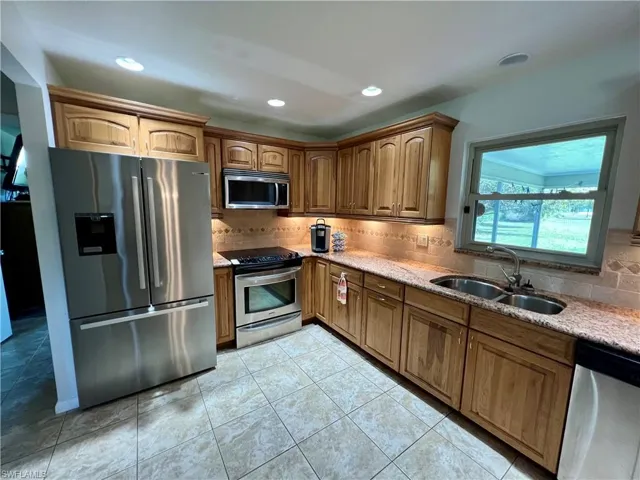 Kitchen featuring decorative backsplash, sink, light GRANITE counters, and appliances with stainless steel finishes