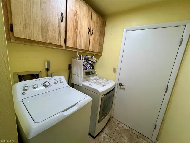 Washroom featuring washer and dryer, light tile patterned floors, and cabinets