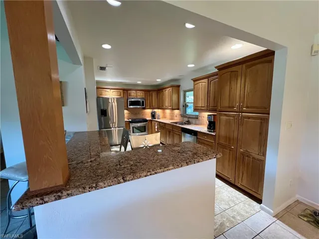 Kitchen with appliances with stainless steel finishes, a breakfast bar, sink, light tile patterned floors, GRANITE countertops