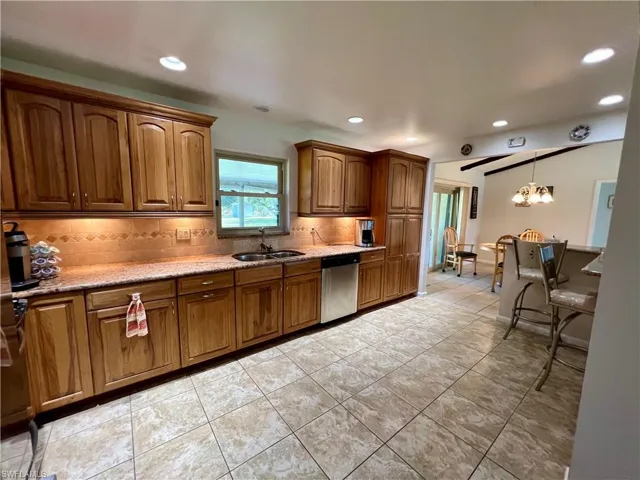 Kitchen with stone tile backsplash, sink, an inviting chandelier, dishwasher, and light tile patterned flooring