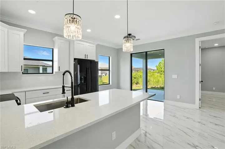 Kitchen featuring black fridge with ice dispenser, a chandelier, ornamental molding, healthy amount of natural light, and recessed lighting