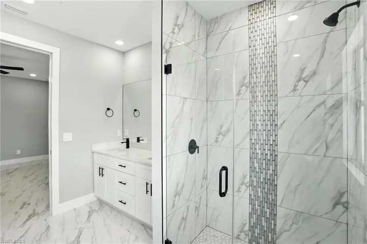 Full bath featuring a marble finish shower, marble finish flooring, double vanity, and recessed lighting