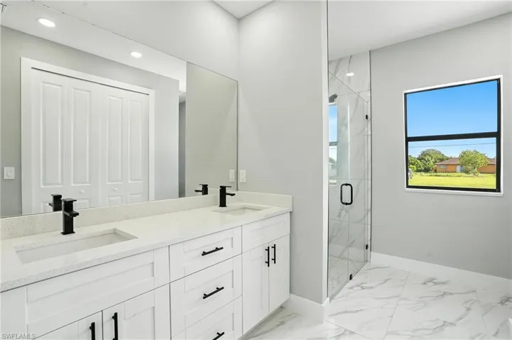 Full bath with marble look tile flooring, a marble finish shower, double vanity, and recessed lighting