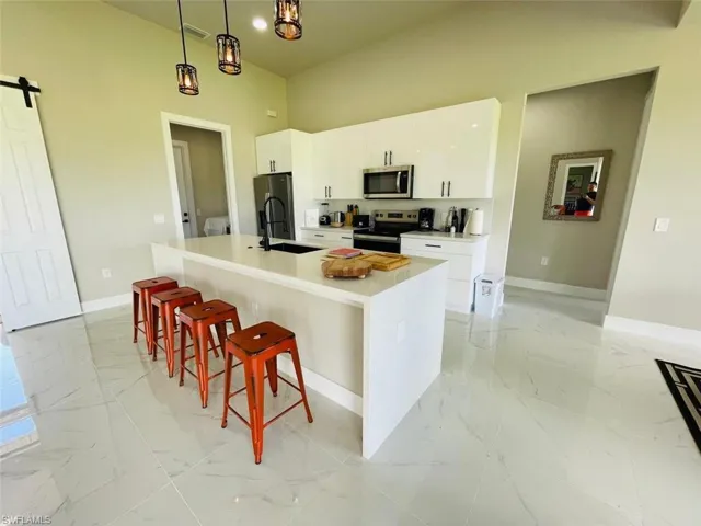 Kitchen featuring a barn door, light marble finish floors, a breakfast bar, and a kitchen island with sink