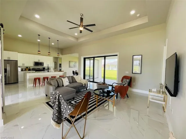 Living room with a tray ceiling, light marble finish flooring, recessed lighting, and a ceiling fan
