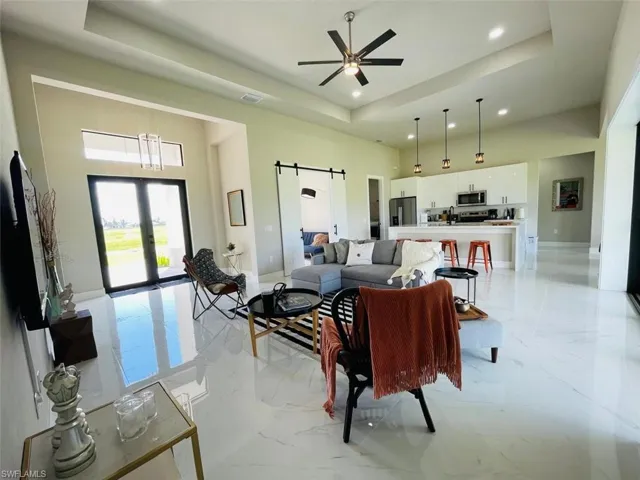 Living room with a tray ceiling, a barn door, light marble finish floors, a towering ceiling, and recessed lighting