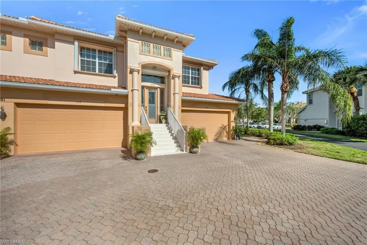 Front exterior with paver driveway, two-car garage, and tropical landscaping.