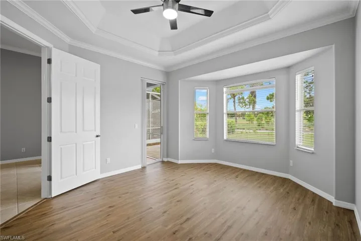 Unfurnished bedroom featuring a raised ceiling, multiple windows, and wood-type flooring