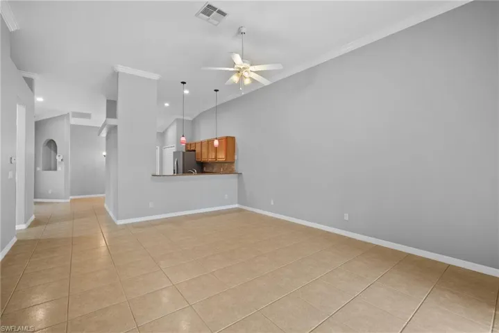 Unfurnished living room featuring light tile patterned flooring, vaulted ceiling, crown molding, and ceiling fan