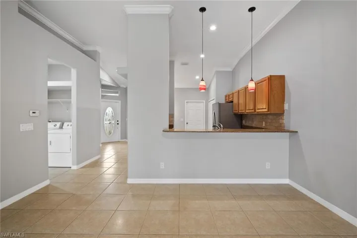 Kitchen with washer and dryer, crown molding, light tile patterned floors, kitchen peninsula, and stainless steel fridge
