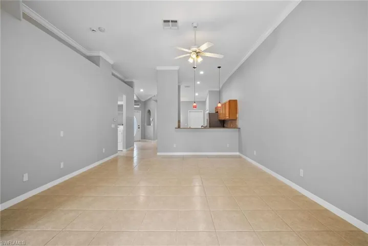 Unfurnished living room featuring ceiling fan, ornamental molding, and light tile patterned floors