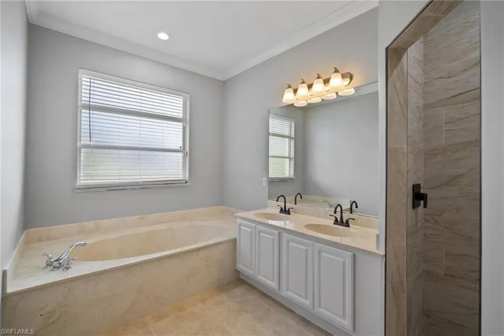 Bathroom with tile patterned flooring, a washtub, crown molding, and double vanity