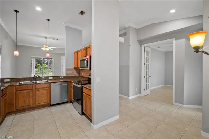 Kitchen with light tile patterned flooring, backsplash, appliances with stainless steel finishes, ceiling fan, and hanging light fixtures