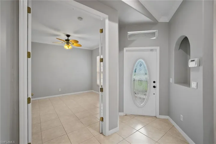 Tiled entrance foyer with ceiling fan and crown molding