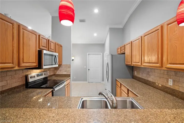 Kitchen with backsplash, sink, ornamental molding, light tile patterned floors, and stainless steel appliances