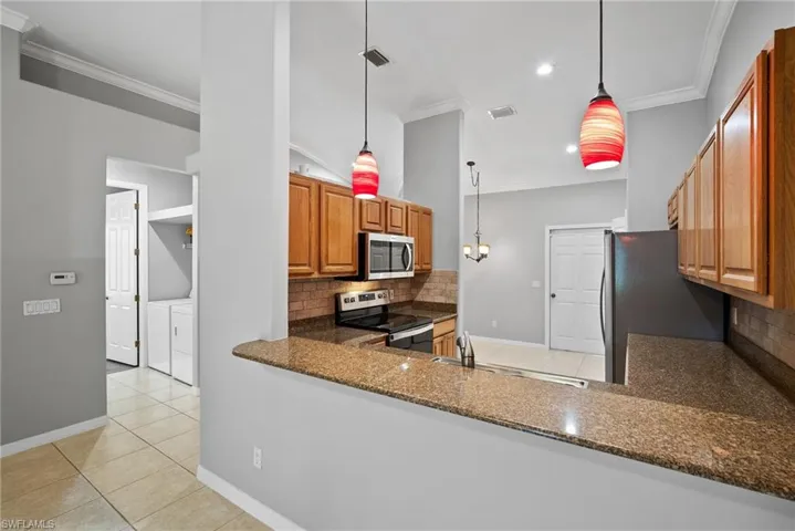 Kitchen featuring appliances with stainless steel finishes, tasteful backsplash, crown molding, washing machine and clothes dryer, and pendant lighting
