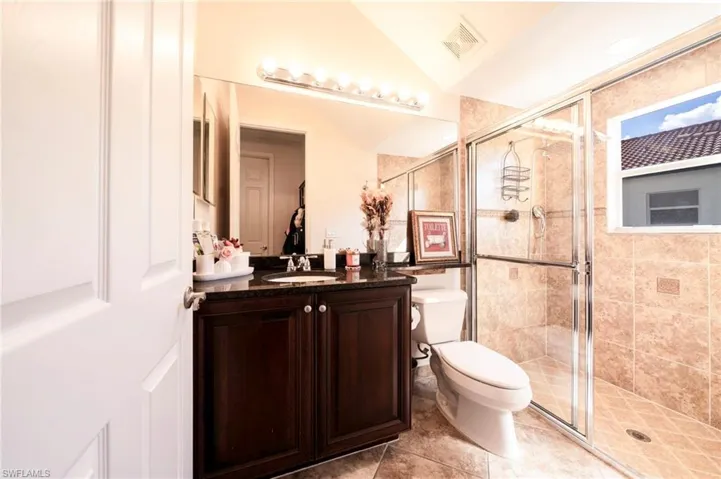 Full bath with vanity, a stall shower, lofted ceiling, and light tile patterned floors