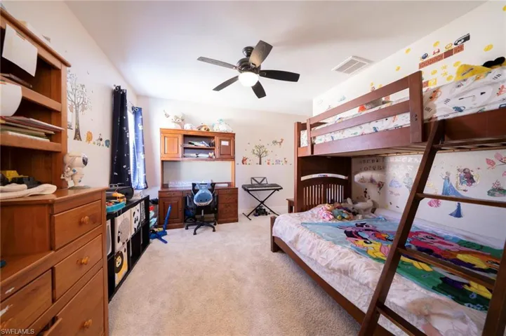 Bedroom with light colored carpet, ceiling fan, and an office area