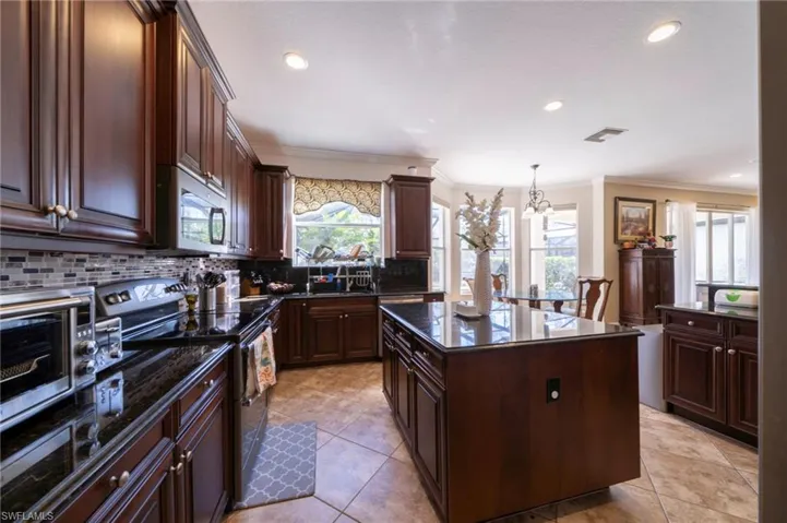 Kitchen featuring range with electric cooktop, dark wood finish cabinets, stainless steel microwave, ornamental molding, and dark stone counters