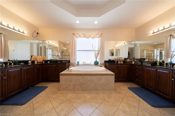 Full bath with a shower stall, two vanities, a garden tub, light tile patterned flooring, and a tray ceiling