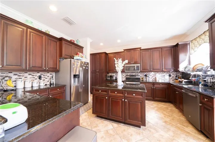 Kitchen with dark stone counters, stainless steel appliances, a kitchen island, dark wood finish cabinets, and light tile patterned floors