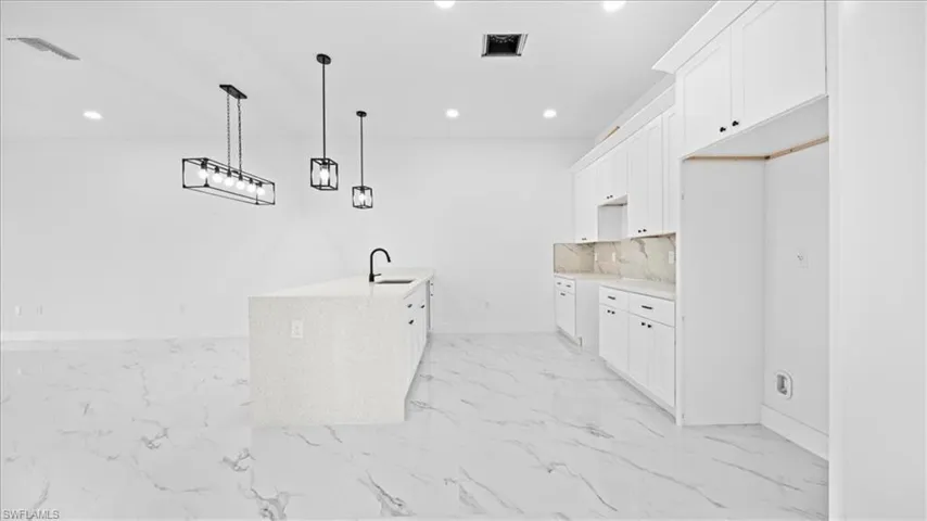 Kitchen with white cabinetry, light stone countertops, recessed lighting, decorative light fixtures, and light marble finish floors