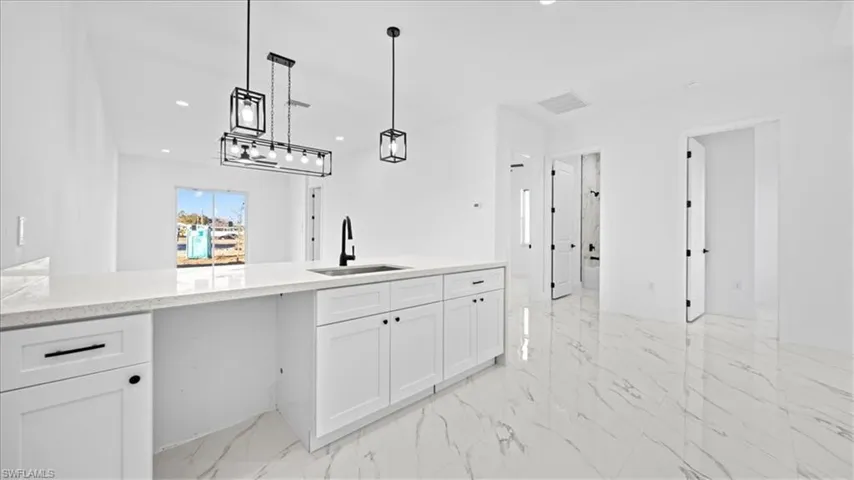Kitchen featuring light stone counters, decorative light fixtures, white cabinetry, recessed lighting, and a peninsula